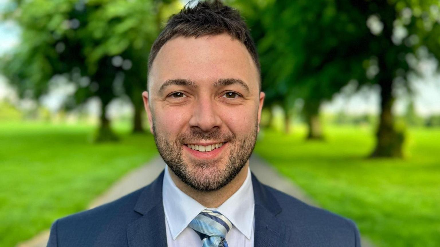 Dan Bennett with short dark hair and beard wearing a blue jacket and tie