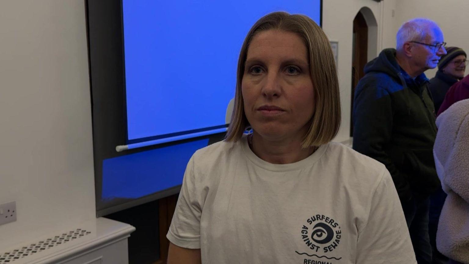 Chani Courtney, wearing a white t-shirt with a round 'Surfers Against Sewage' logo, standing alongside a blue projector screen