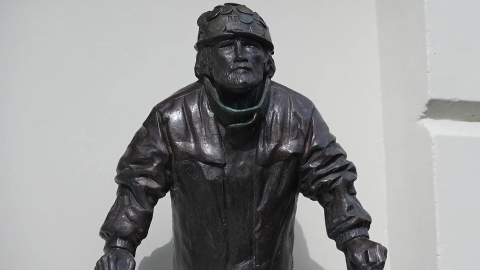 A bronze statue of Brian Haw wearing a hat and jacket.