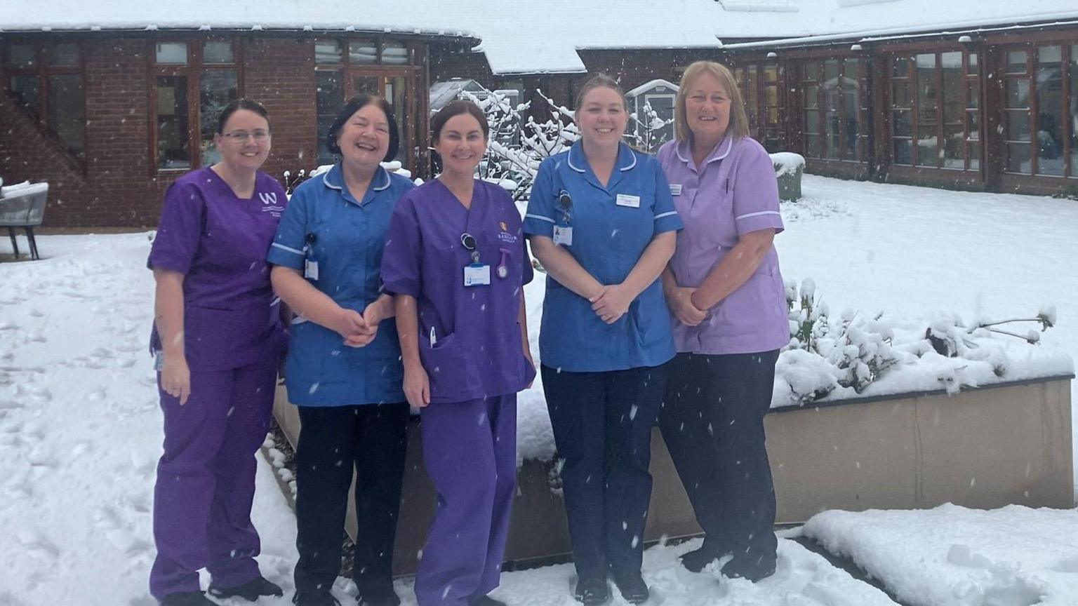 Five women, all dressed in nursing uniforms. stand in the snow covered courtyard of Nightingale House Hospice