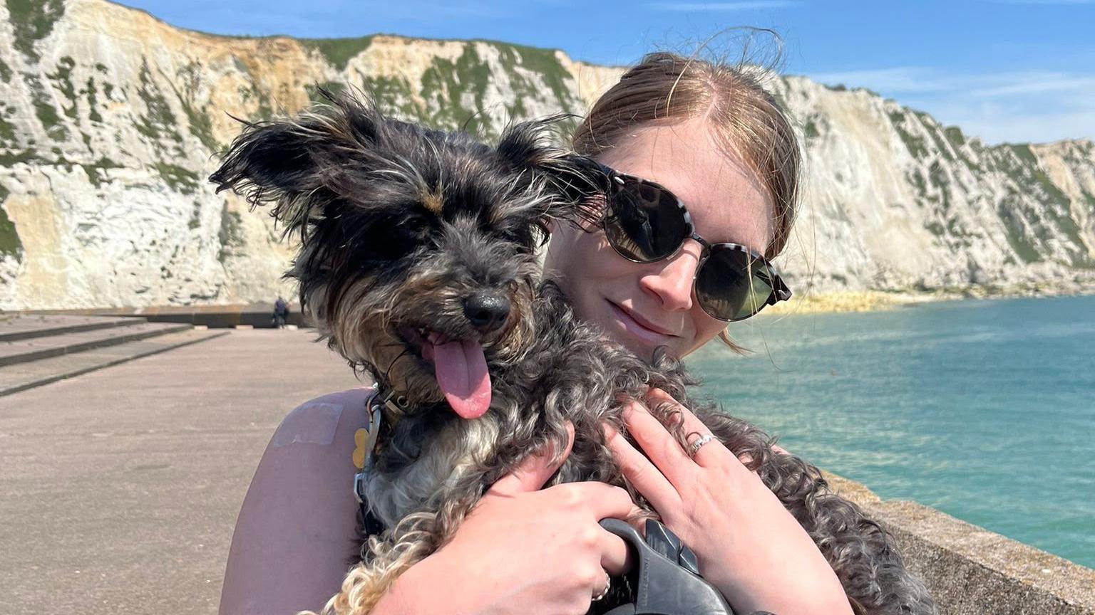 Sophie O'Sheen holding a dog in front of some cliffs and the sea