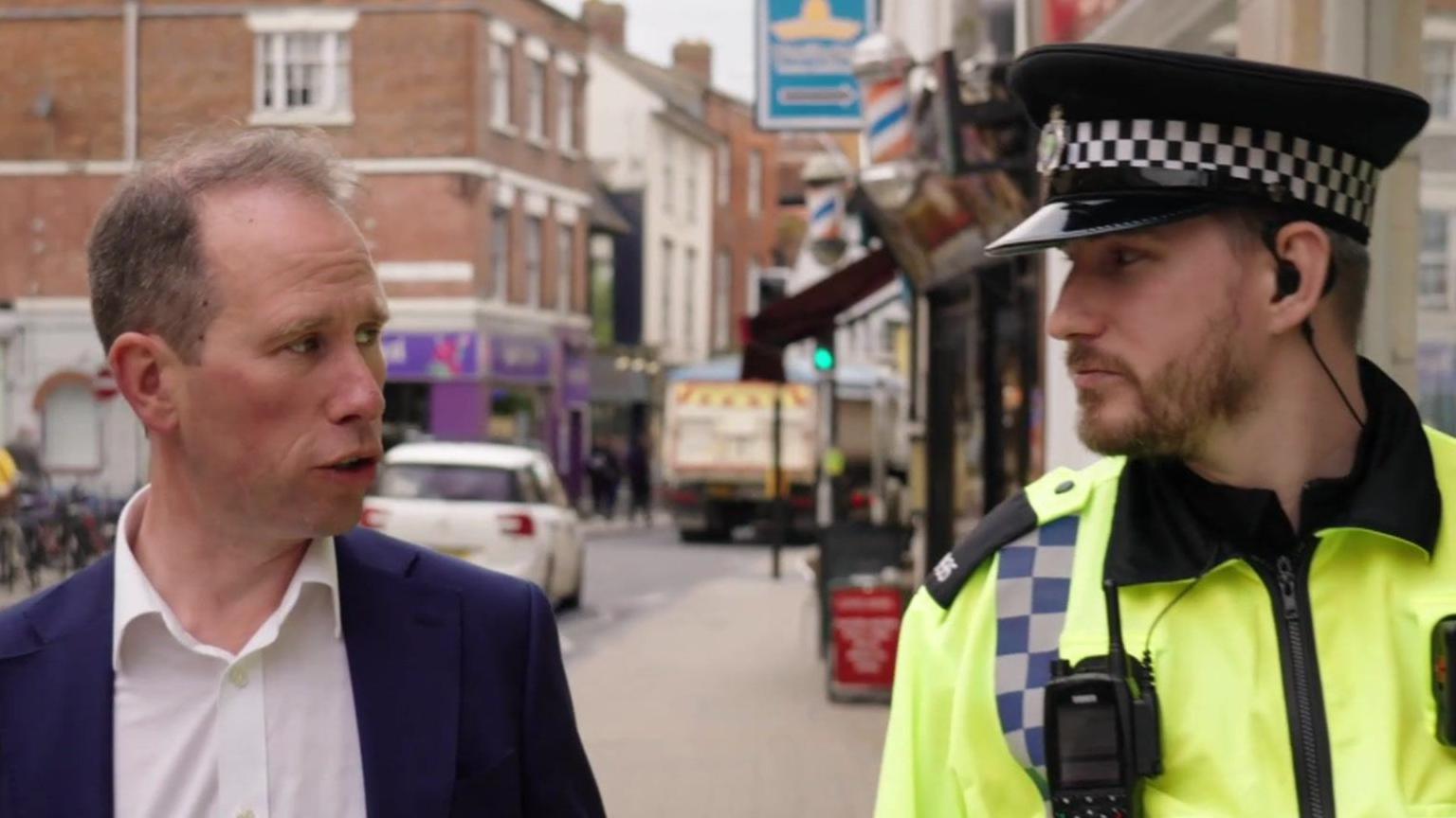 Mr Barber on the left is talking to a policeman on the right. Behind them is a busy high street.