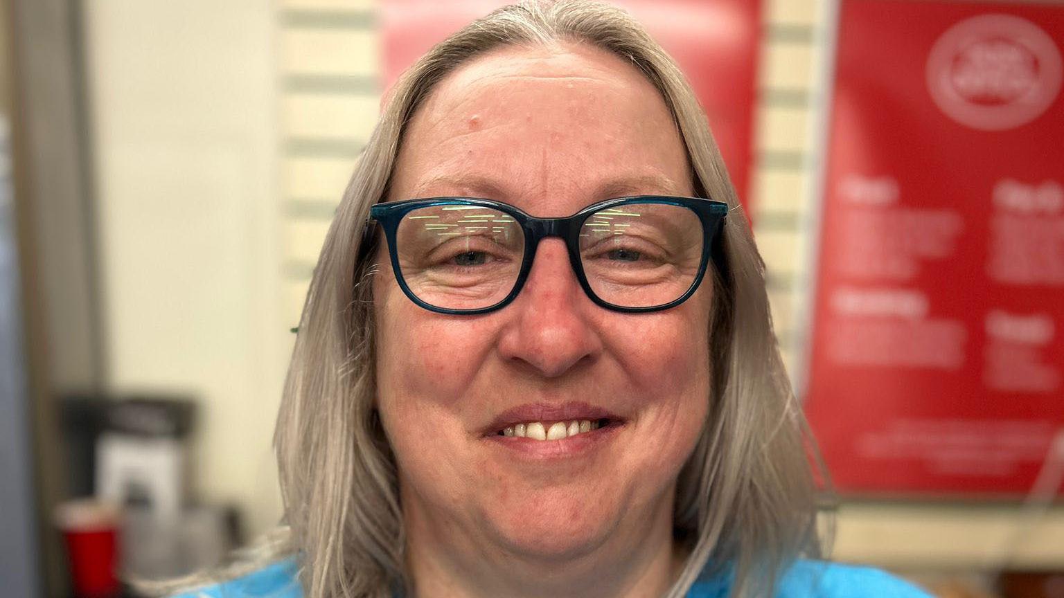 A blonde-haired woman in a blue T-shirt with glasses