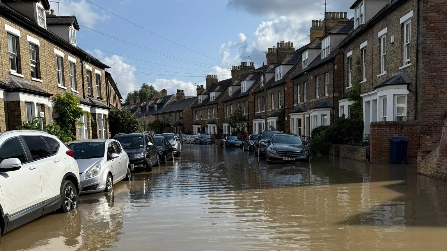 A street in Oxford with water reaching the base of most cars parked on either side.