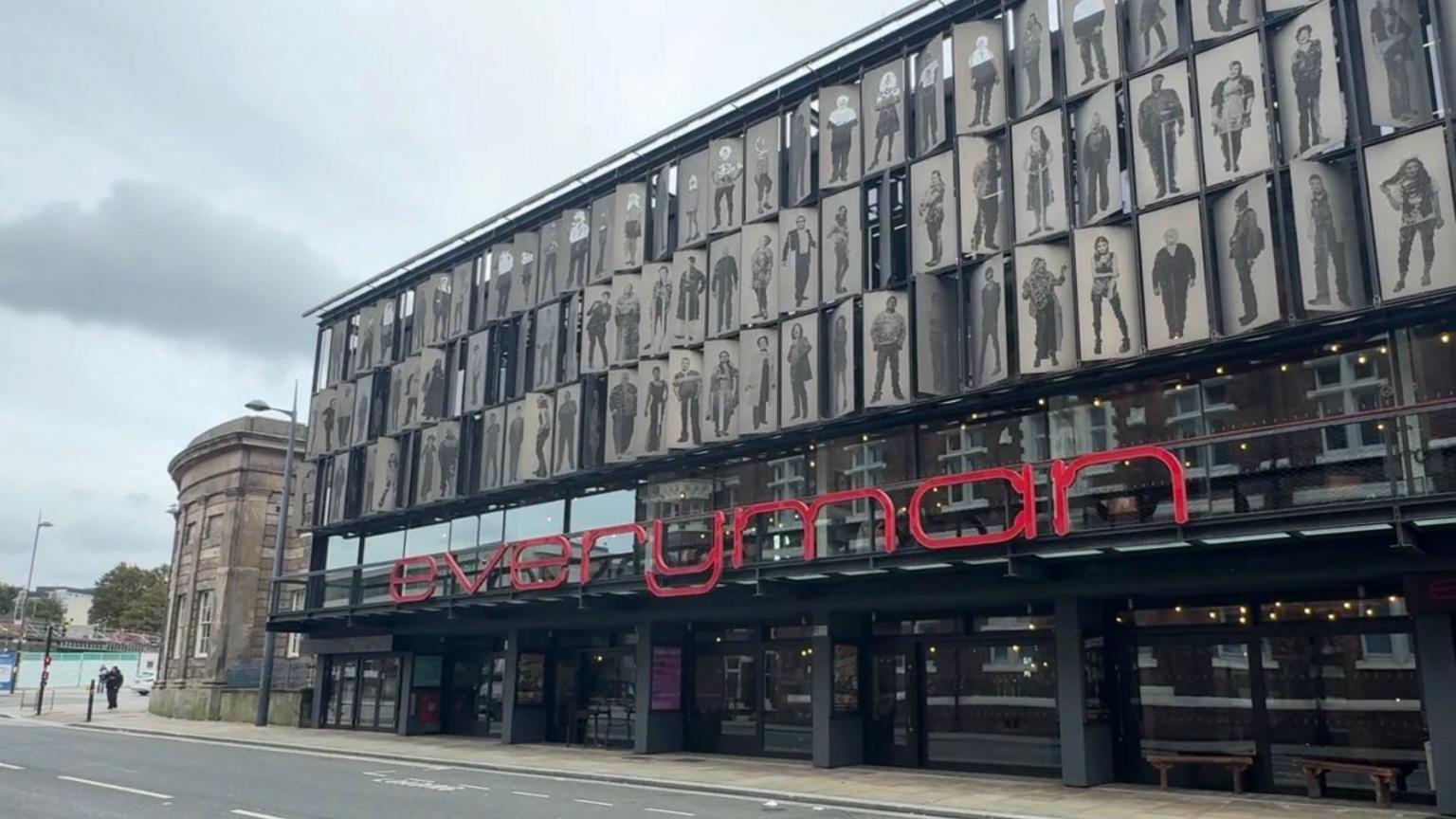 A building with red signage titled 'everyman' behind the sign is pictures of stars.