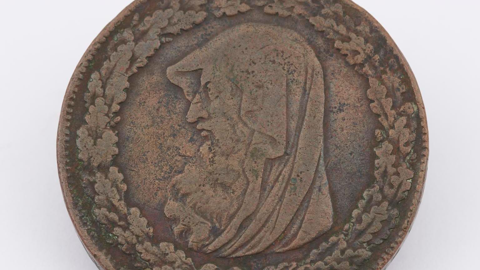 A bronze old coin, with a artwork of a hooded druid figure with a long beard