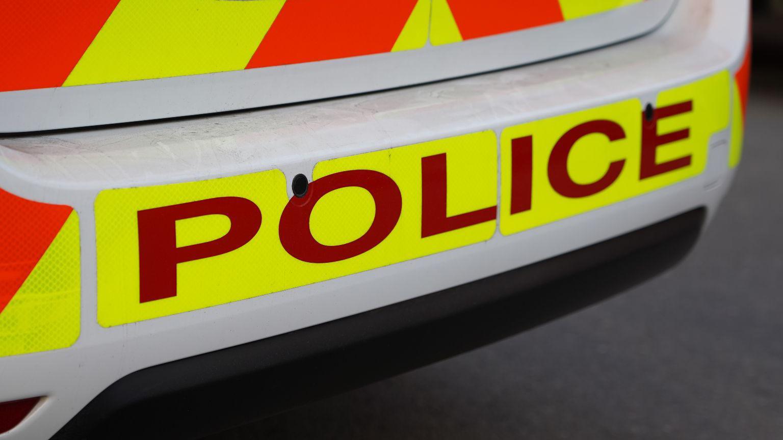 Rear of police car with "police" emblazoned in red on a bright yellow background on the bumper.