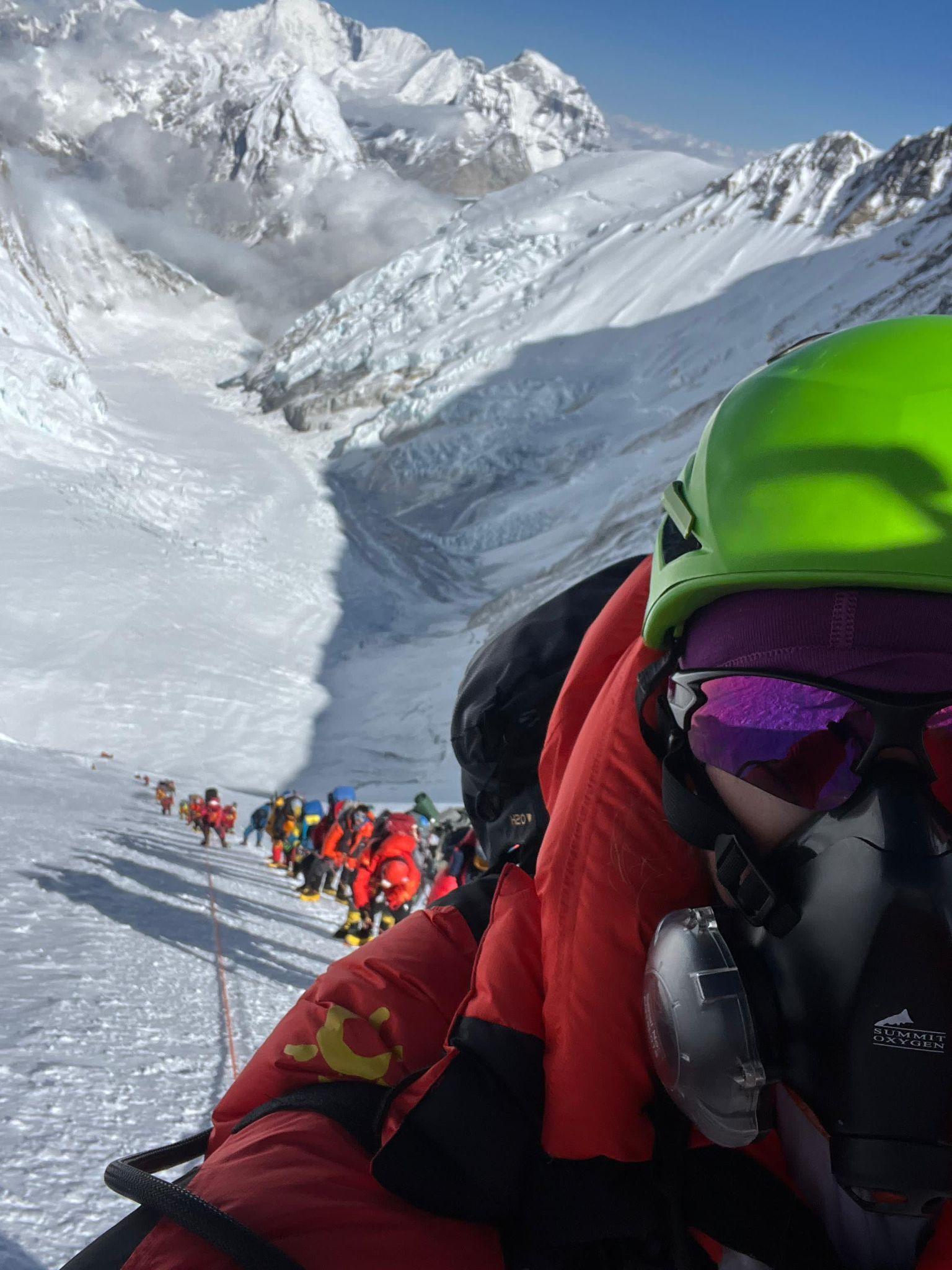 Rowena in full kit, face covered in a line of other climbers