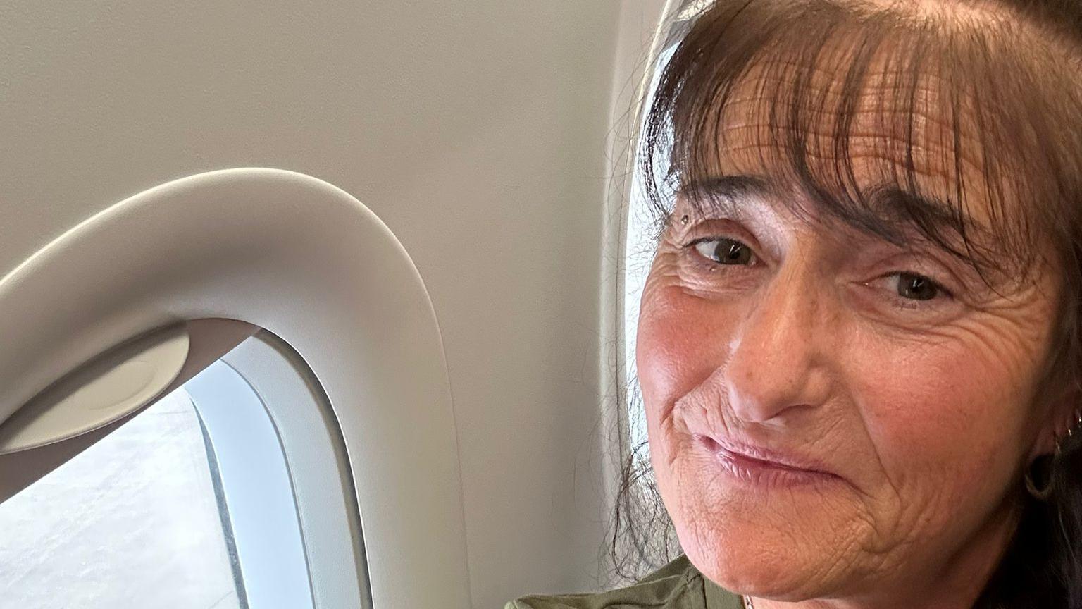 A woman with brown hair looking into the camera while sitting on an aeroplane