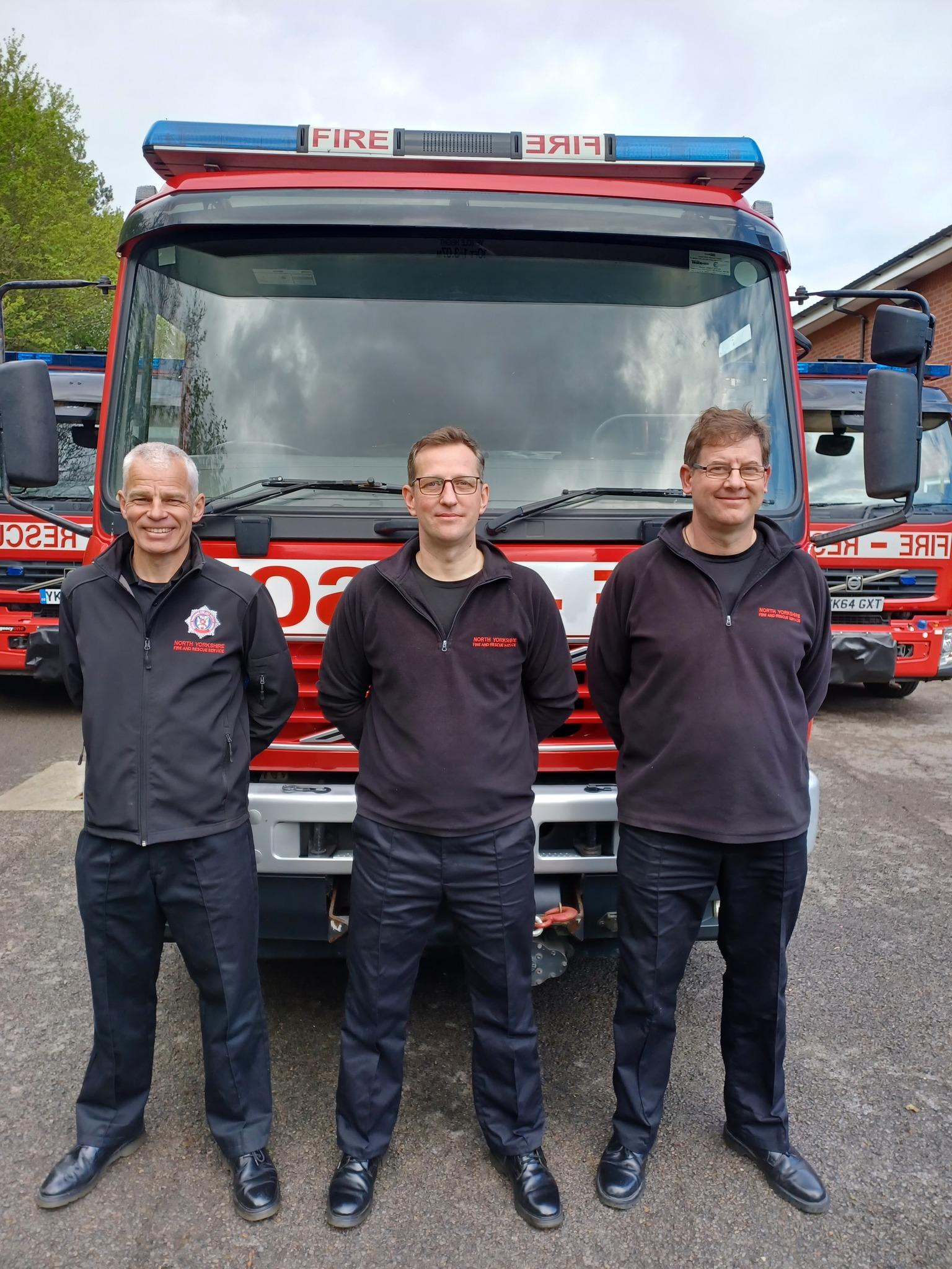 Three fire fighters stand in front of an engine