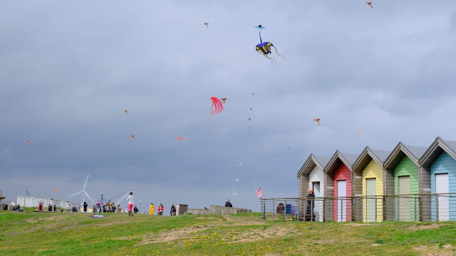 Kites in the sky with lots of people on the brow of a hill 