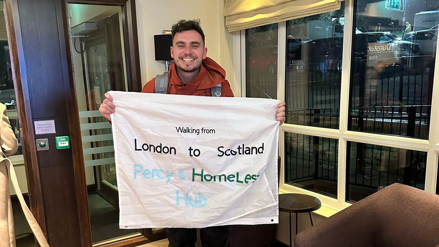 A man smiles holding a banner in advertising a homeless charity. 