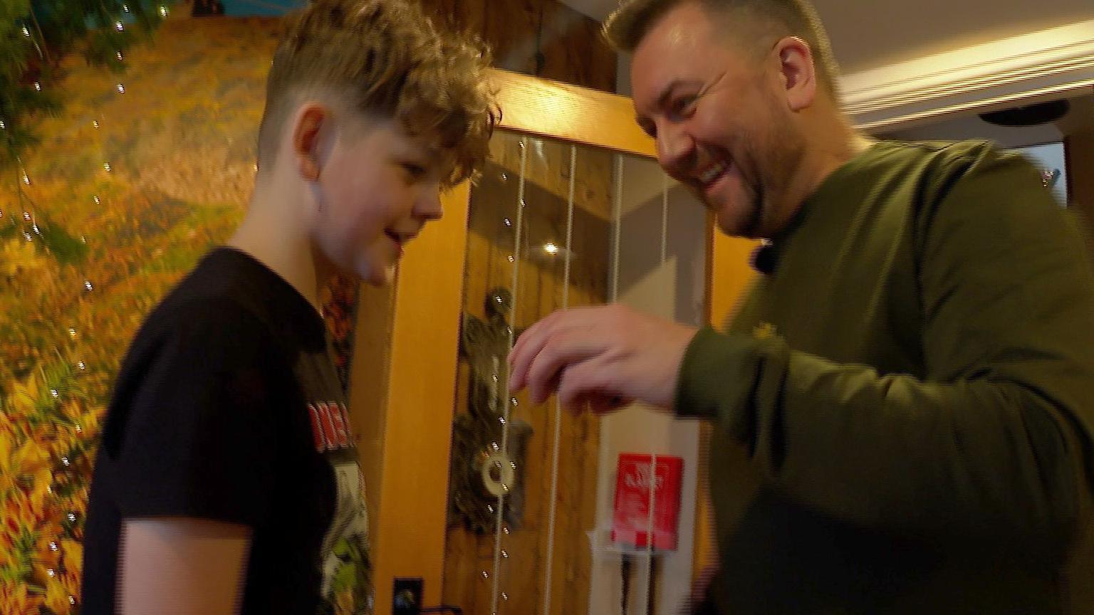 A boy in a black T-shirt with a man with a beard and a green top laughing.