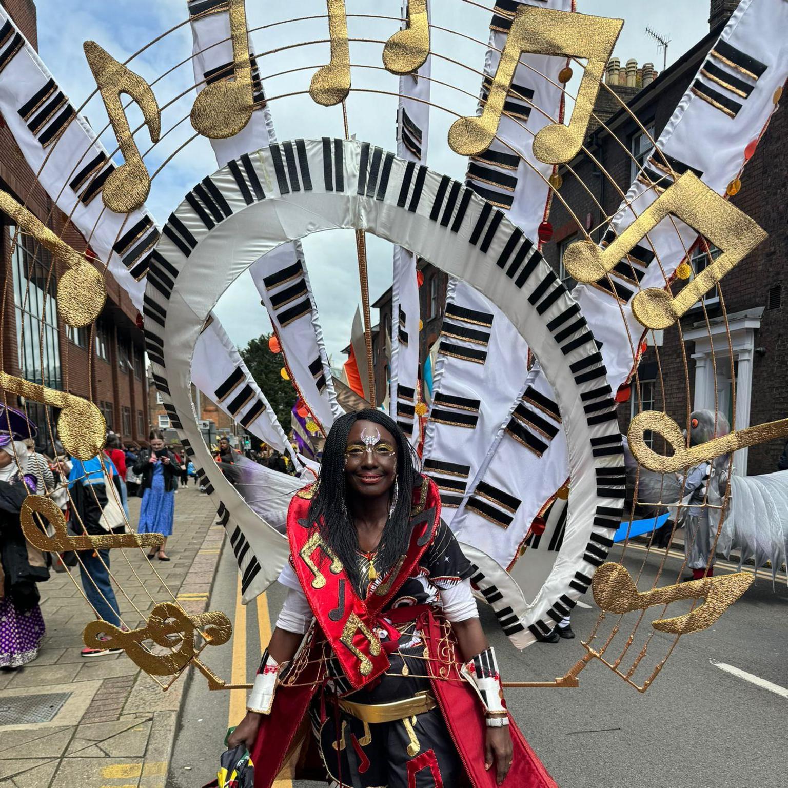 Angela Walters wearing an enormous costume adorned with golden musical notes and piano keyes