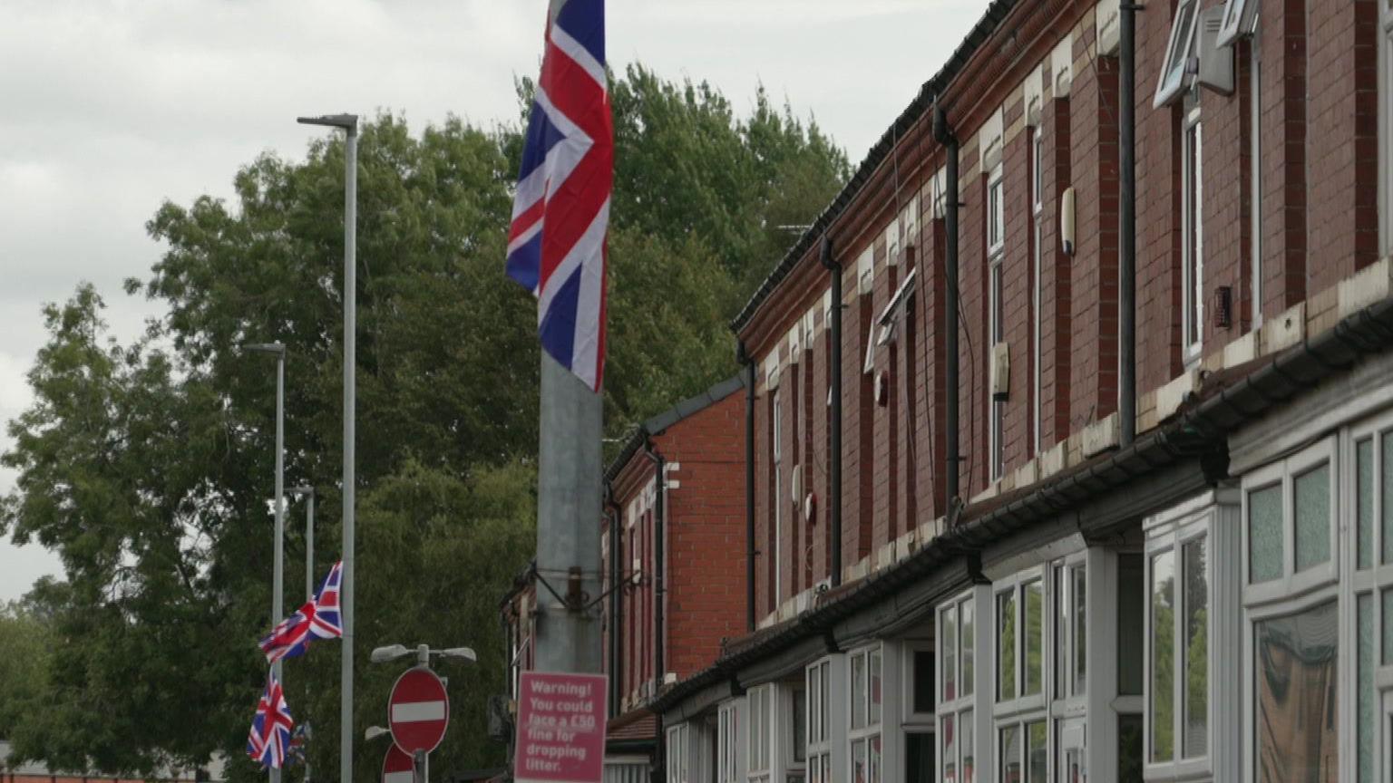 Lampposts with union jack flags hanging from them outside a row of terraced houses.