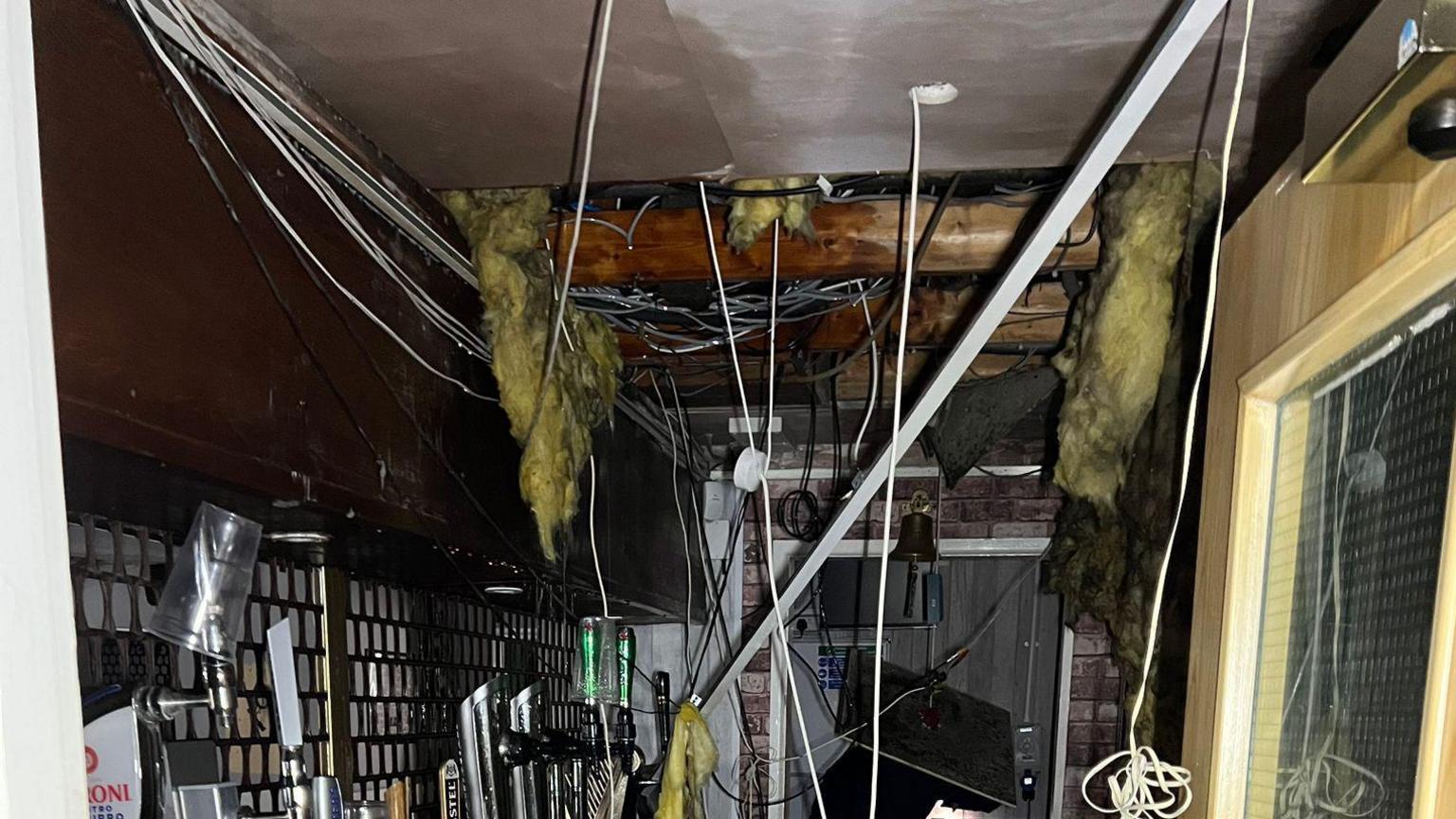 Inside a room where the ceilings have come down with lots of loose wired hanging from the ceiling and insulation