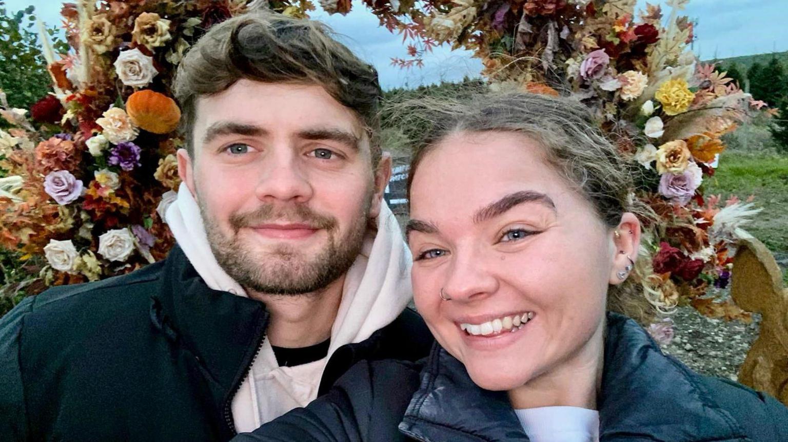 Cori and his girlfriend taking a selfie in front of some flowers