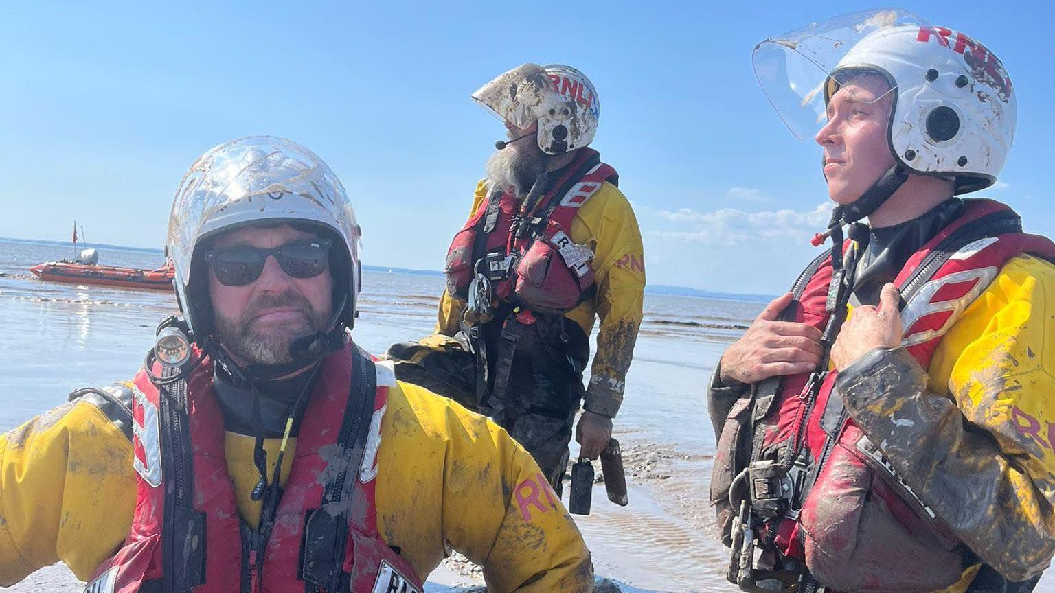 Three Weston RNLI volunteers pictured in the mud during a rescue. They are wearing yellow protective jackets, red life vests and white helmets.
