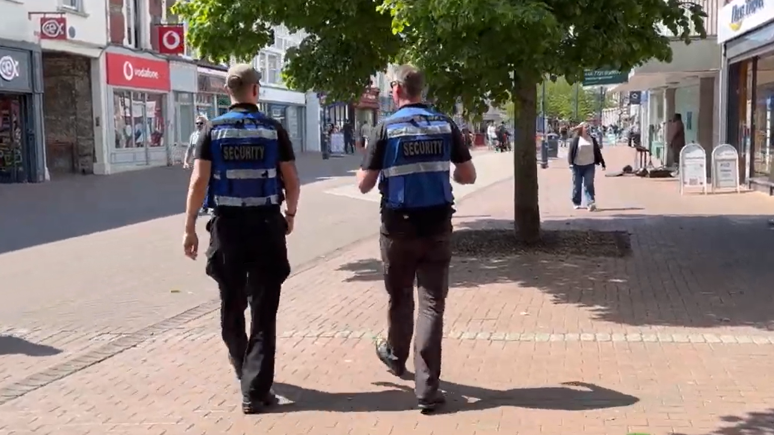 Two uniformed men walk down Gosport's sunny, pedestrianised high street. Their blue high-vis jackets have the word "security" on the back.