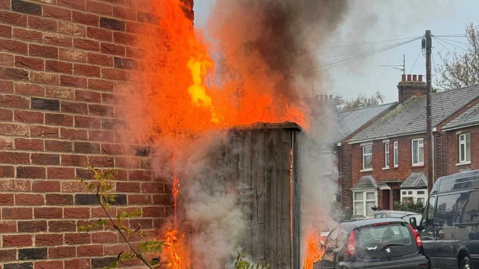 Flames and smoke rise from a fence outside a house.