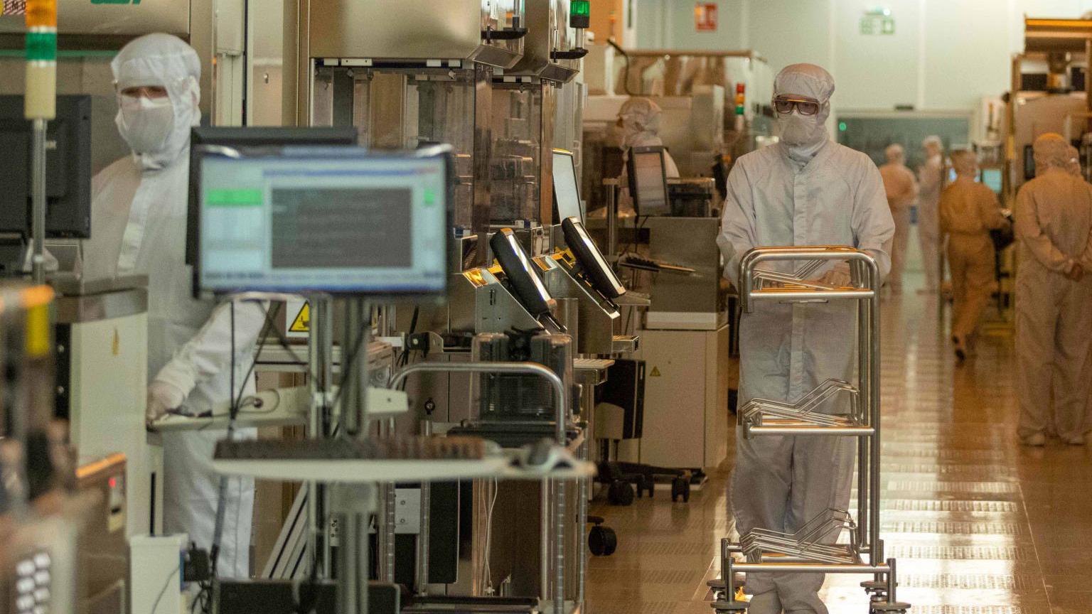 Scientists in white protective clothing are seen working among computers and large machines.