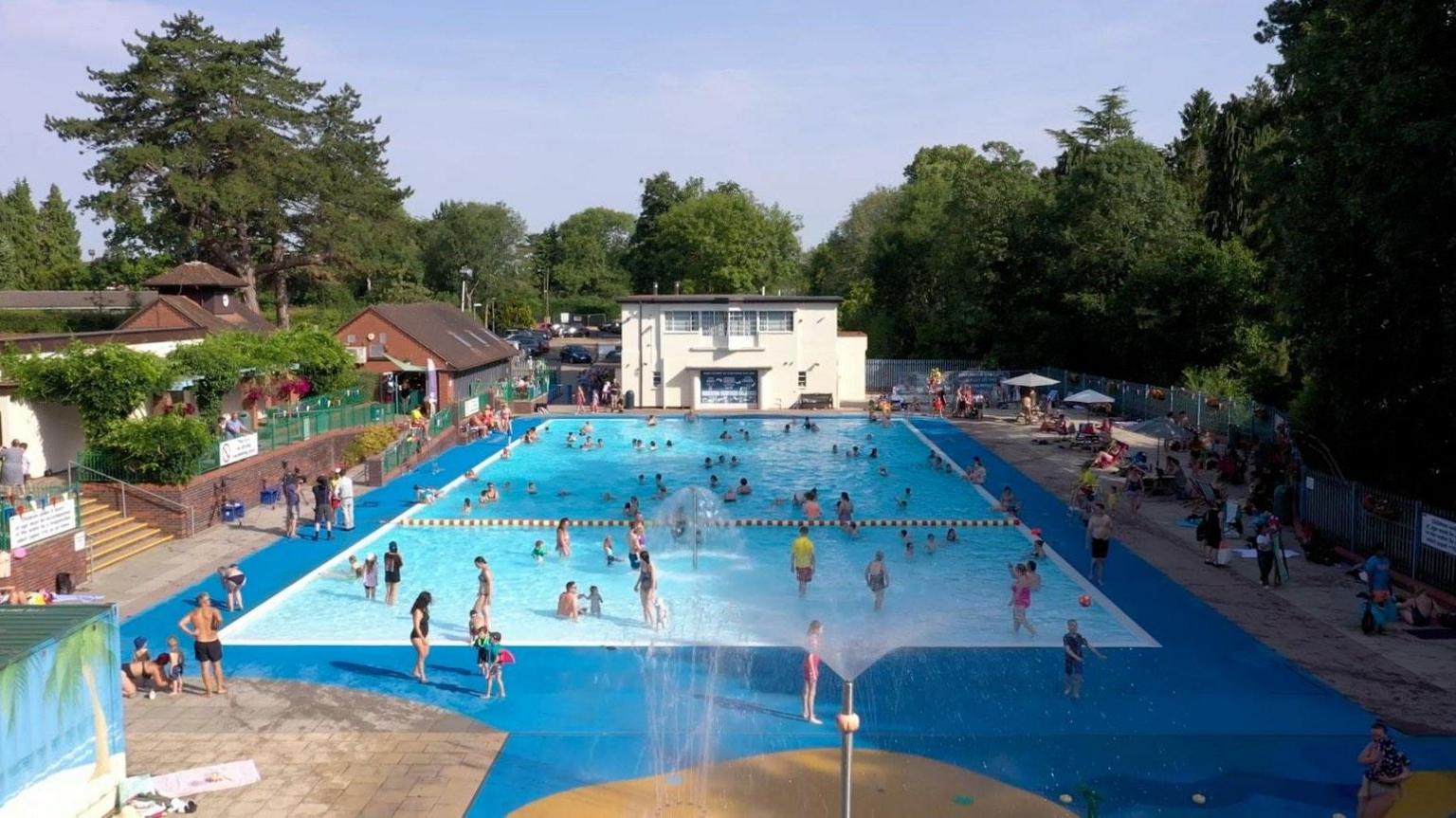 A view of the lido, which opened in 1935 and has been restored. There are people swimming in the pool and standing around it on a sunny day.