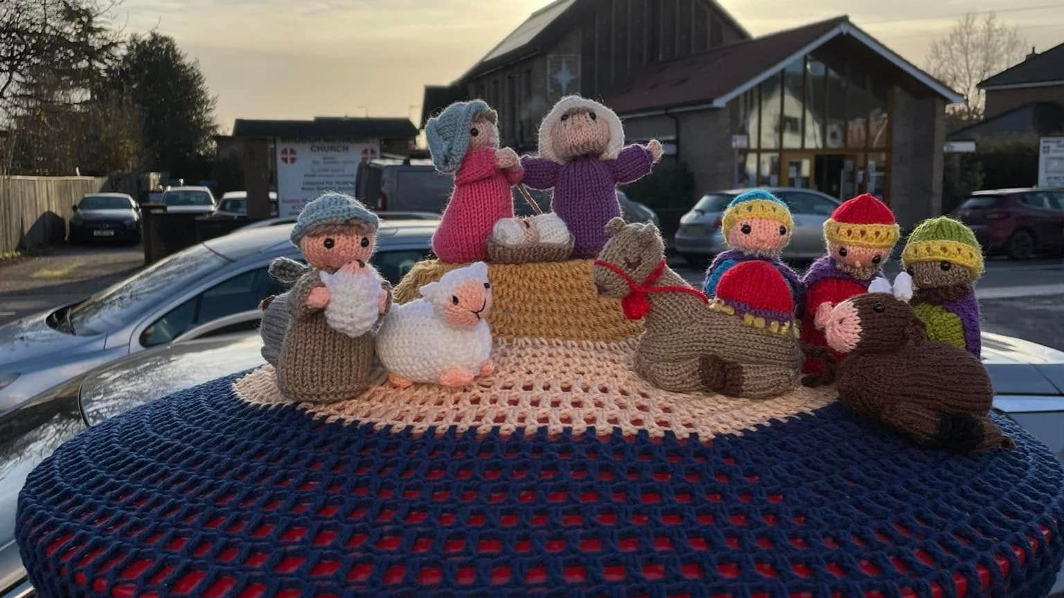 Mary and Joseph, the three wise men, a shepherd and sheep and other animals gather around the knitted baby Jesus on top of a crocheted manger.