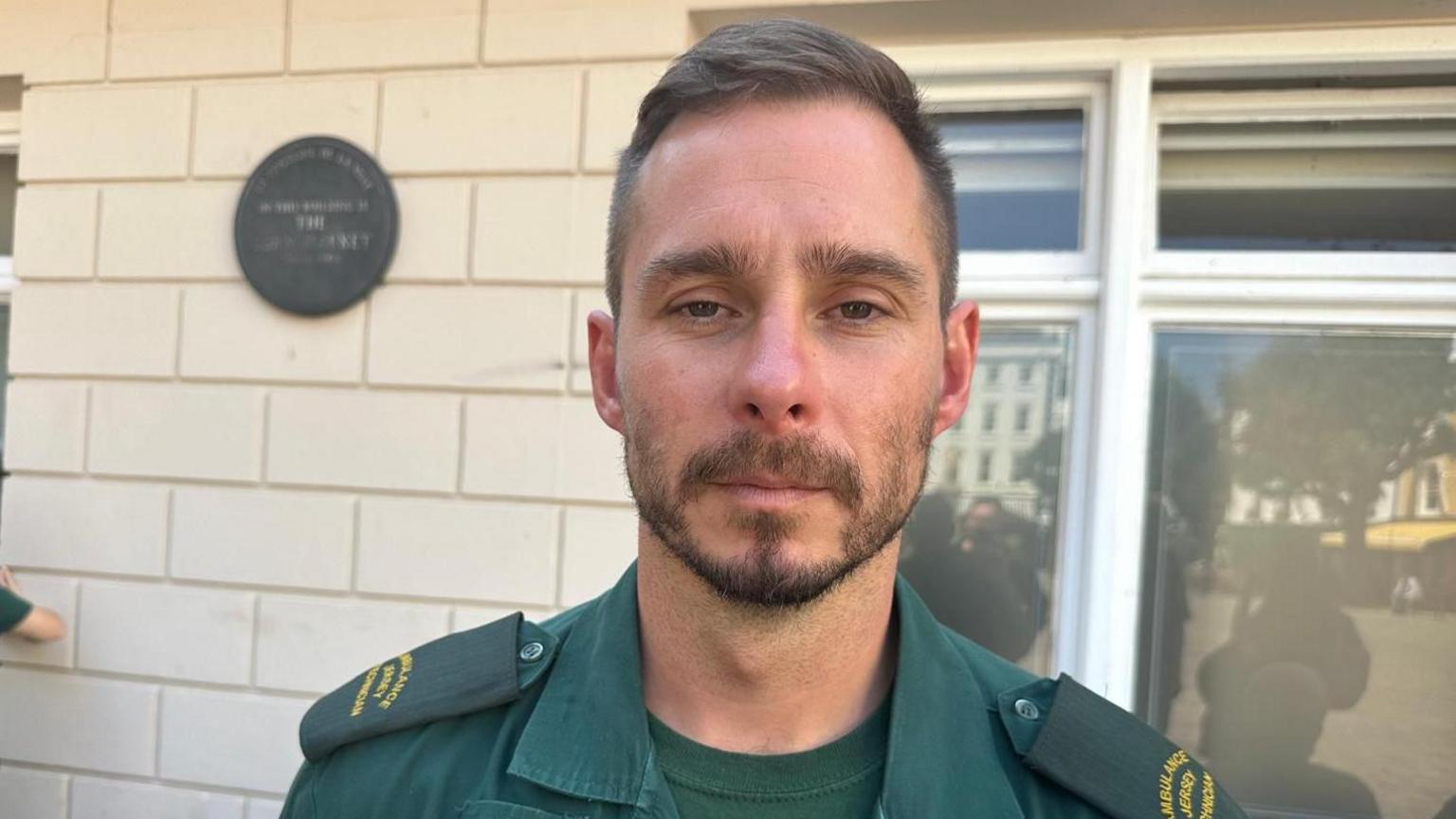 Tom Le Sauteur standing in front of a cream brick wall and window, wearing ambulance uniform.