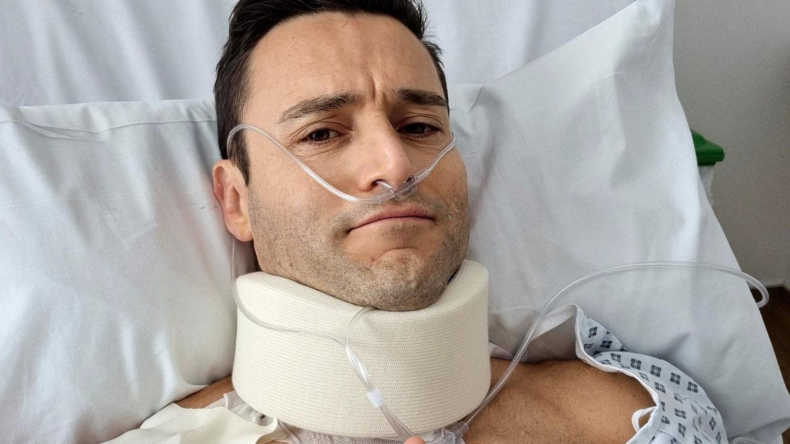 MP Dr Luke Evans in a hospital bed with oxygen tubes and a neck brace