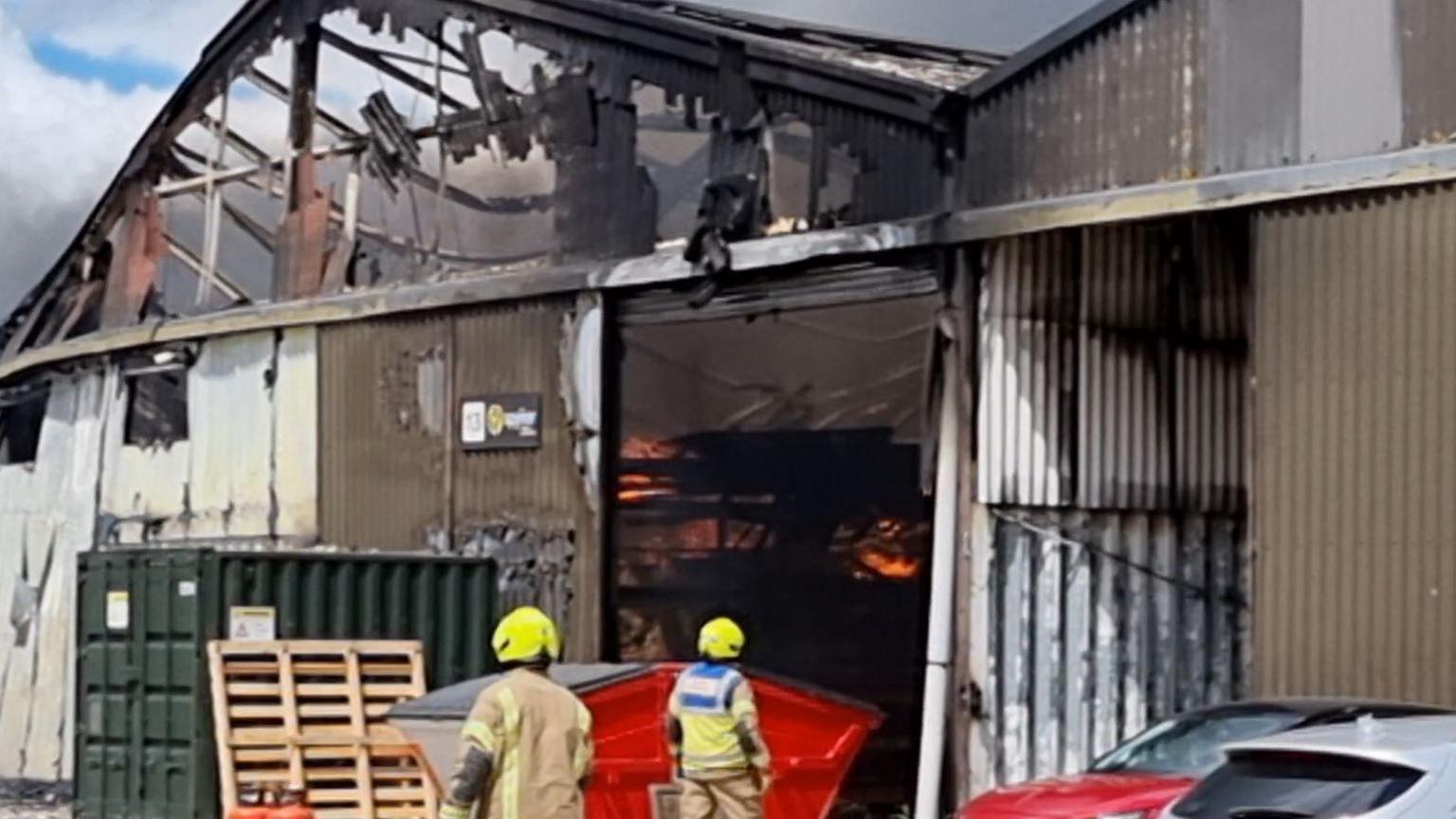 A burned warehouse and firefighters standing outside it