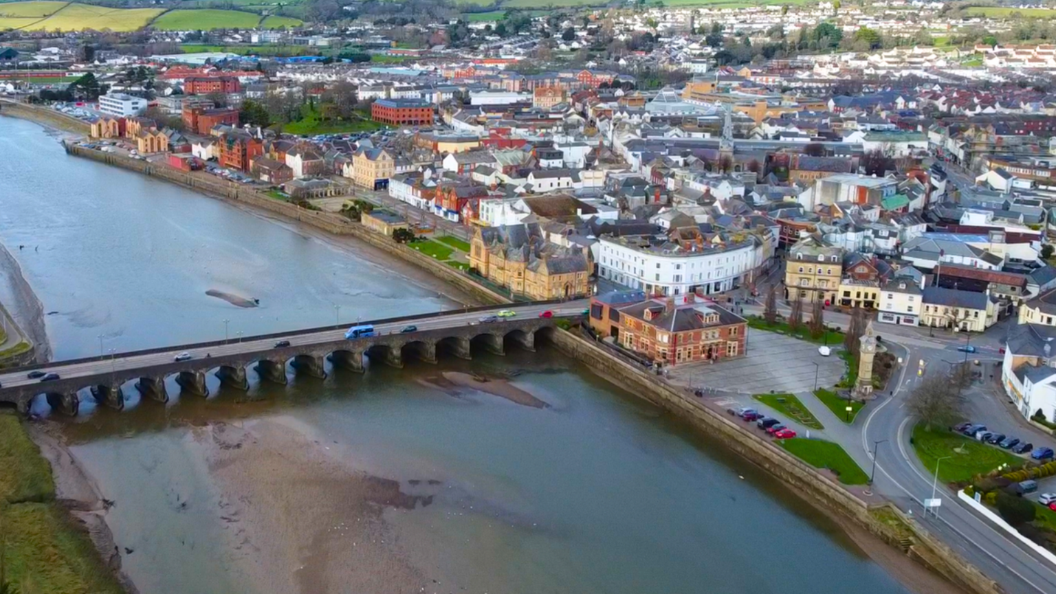 An aerial view of homes and businesses besides the River Taw at Barnstaple. Traffic is crossing the river on a road bridge.