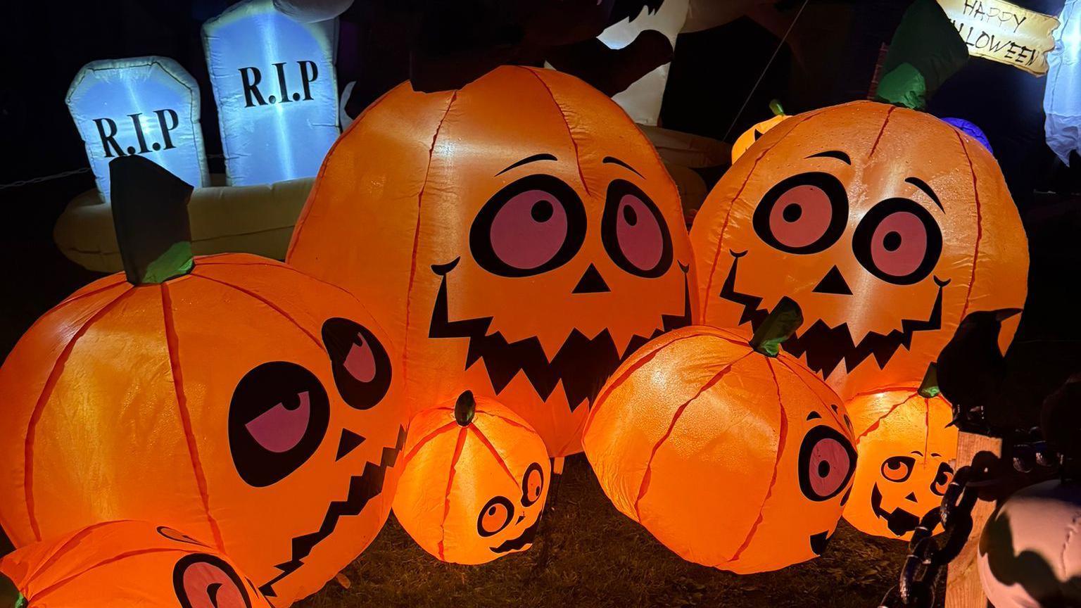 Inflatable orange pumpkins with faces. There are three large pumpkins about the size of a small exercise ball. There are also four small pumpkins ranging from the size of a football to one that is slightly larger. 