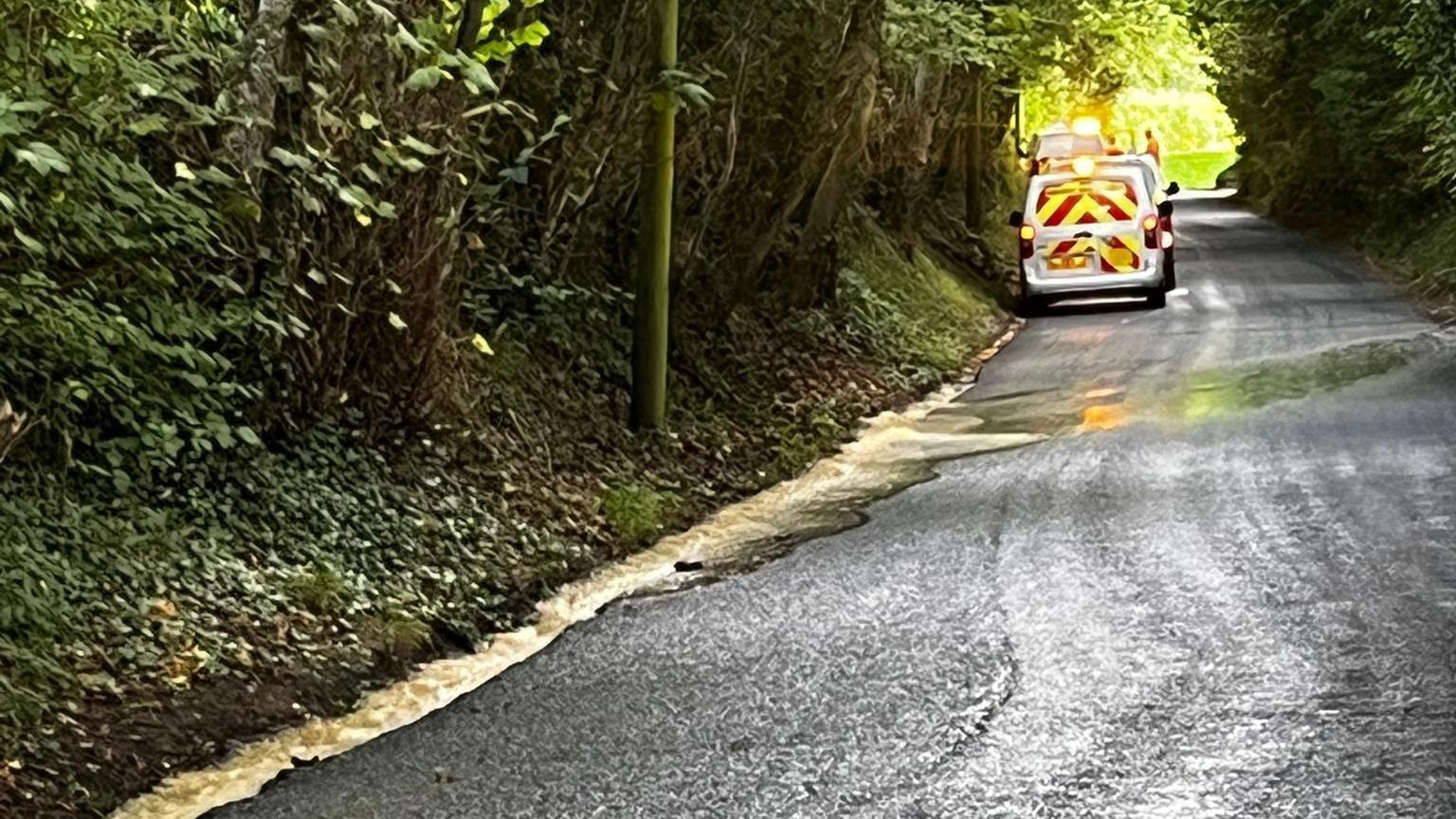 A South East Water van in a country lane in Newick, with water running down the hill.