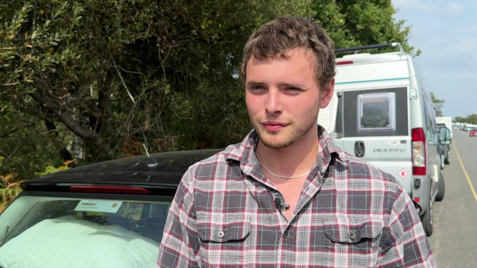 Isaac Beck  with checked shirt, standing by a car, with Ferry Road and other parked cars in the background