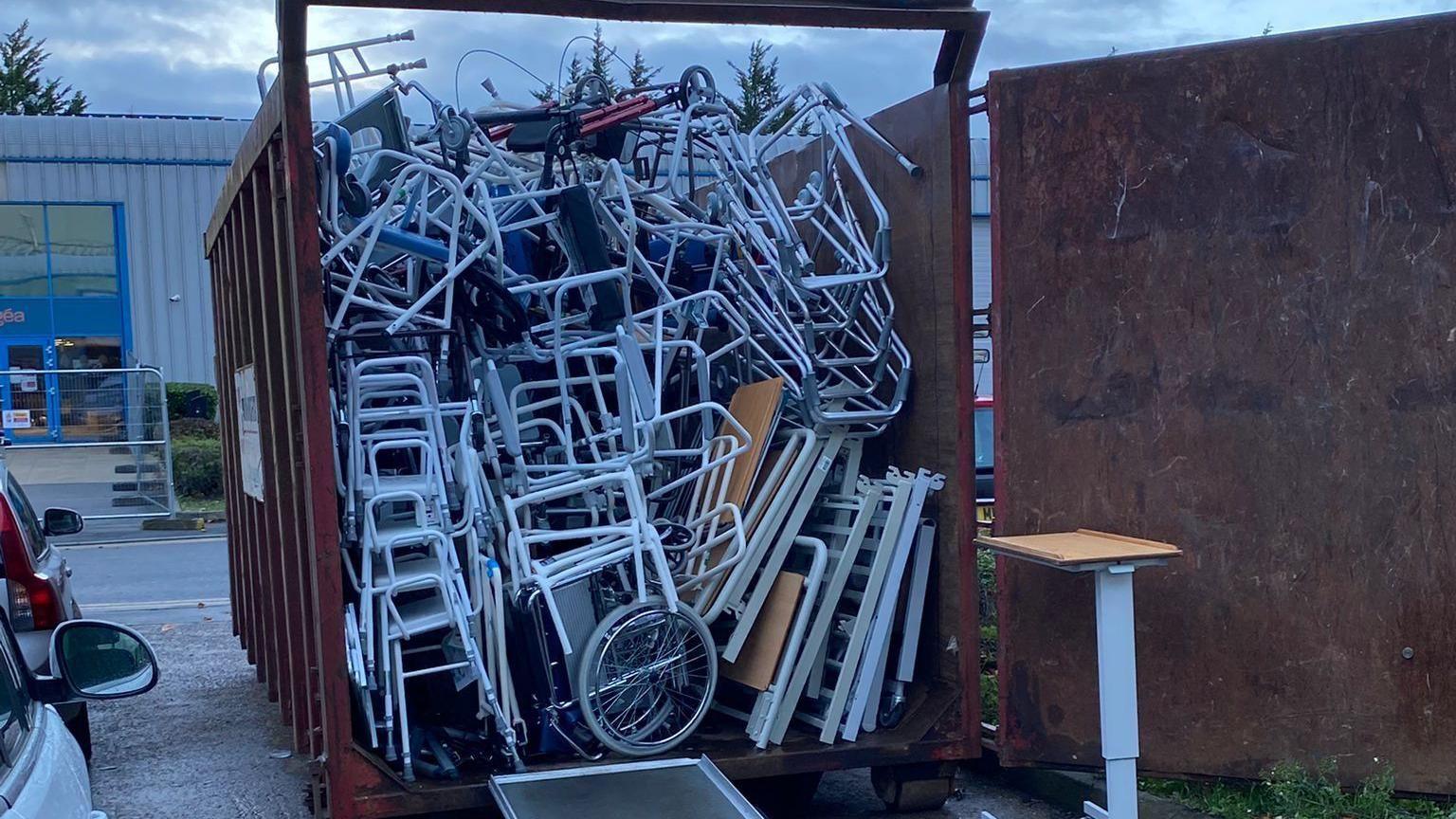 A large stack of wheelchairs, walker and other medical equipment in a metal shipping-container sized bin