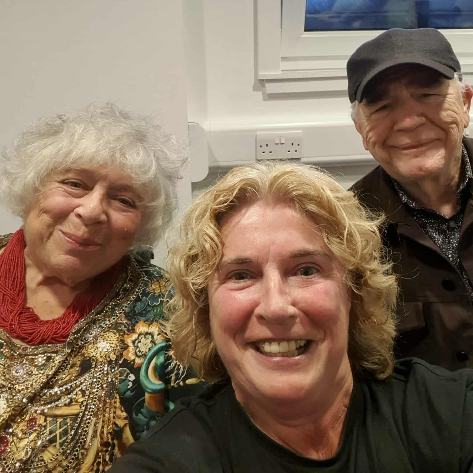 A selfie of Miriam with a gold patterned dress and a red beaded necklace, with comedy critic Gayle Anderson, a blonde woman in a black T-shirt, and Scots actor Brian Cox, in a brown cap, brown jacket and a patterned floral shirt.