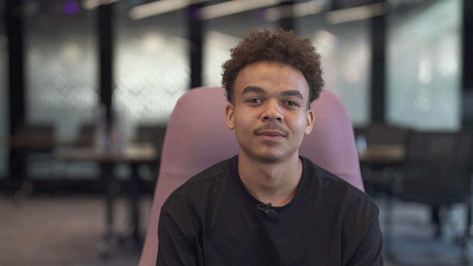 Head and shoulders of a young man looking straight at camera with tables and chairs in the background