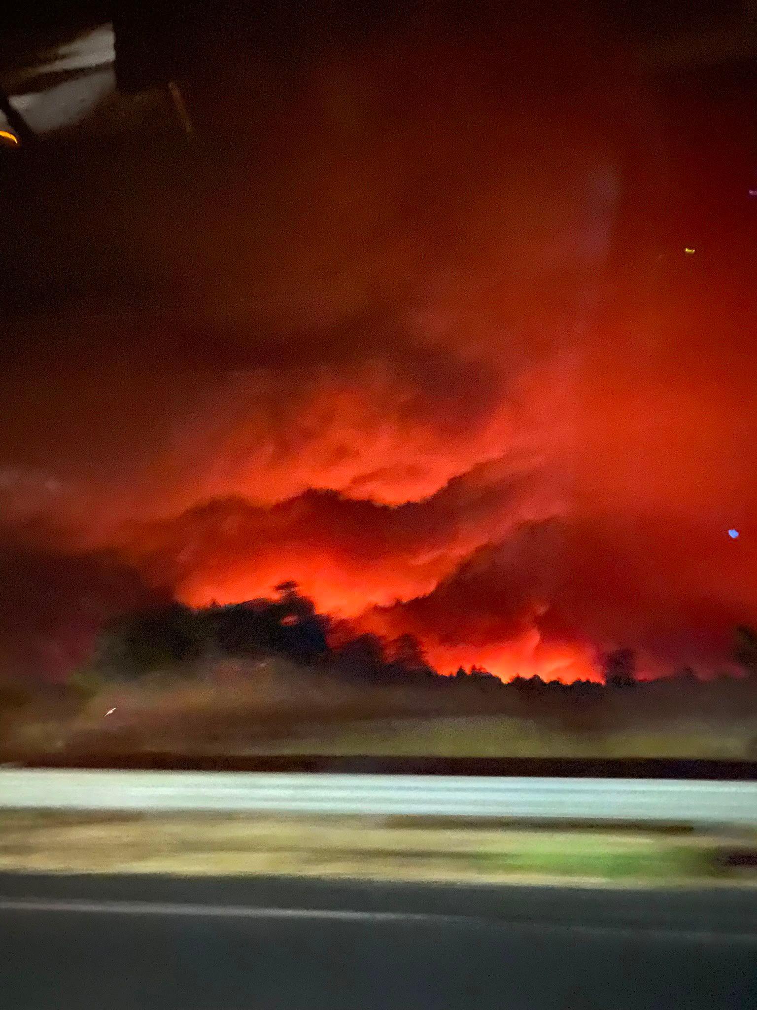 An image taken from the window of a car showing the sky filled with an orange glow from the flames