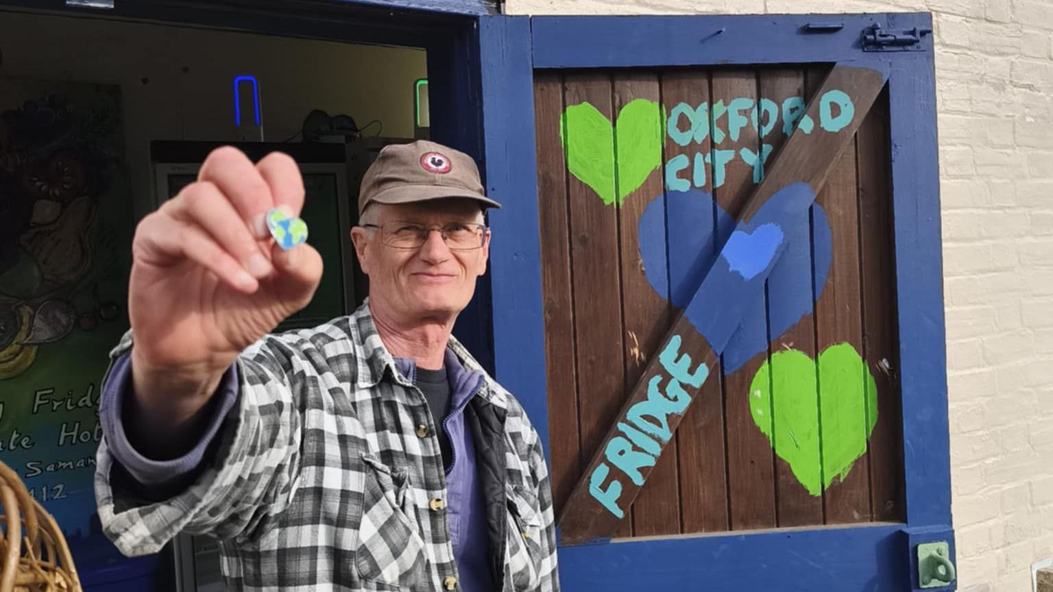 A man smiling for the camera at the event launch and holding a heart-shaped pin with the world map on it.