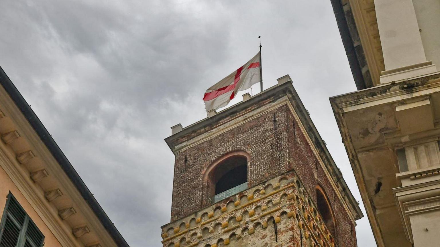 An ornate stone tower with a white flag bearing a red cross flying from the top