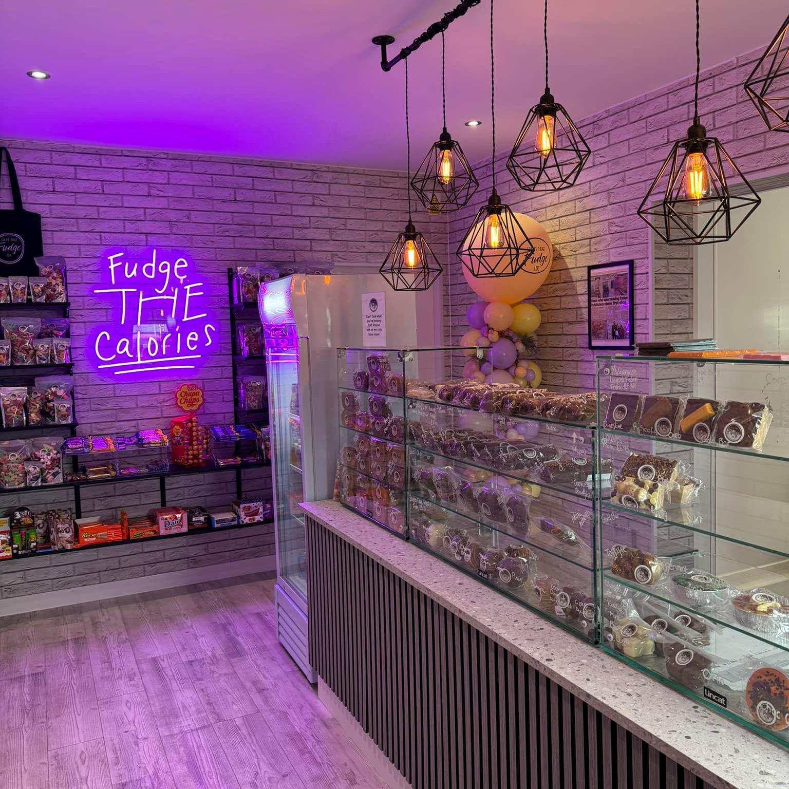 The interior of the Want That Fudge shop in Scunthorpe. There is a neon sign on the wall and shelves featuring a selection of fudge, sweets and chocolate.