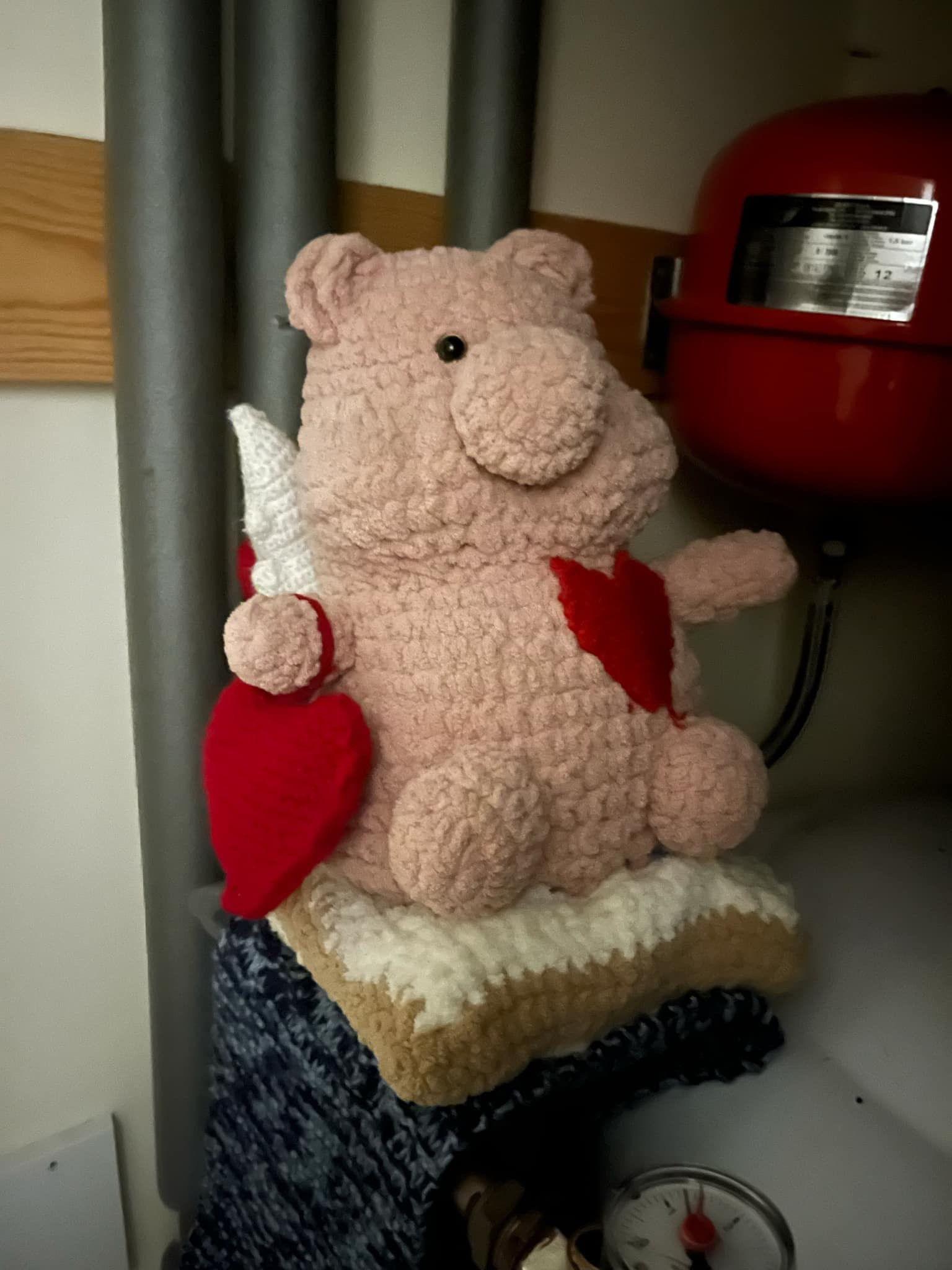 The pig is adorned with hearts to raise money for the British Heart Foundation.  He is sitting on a radiator.