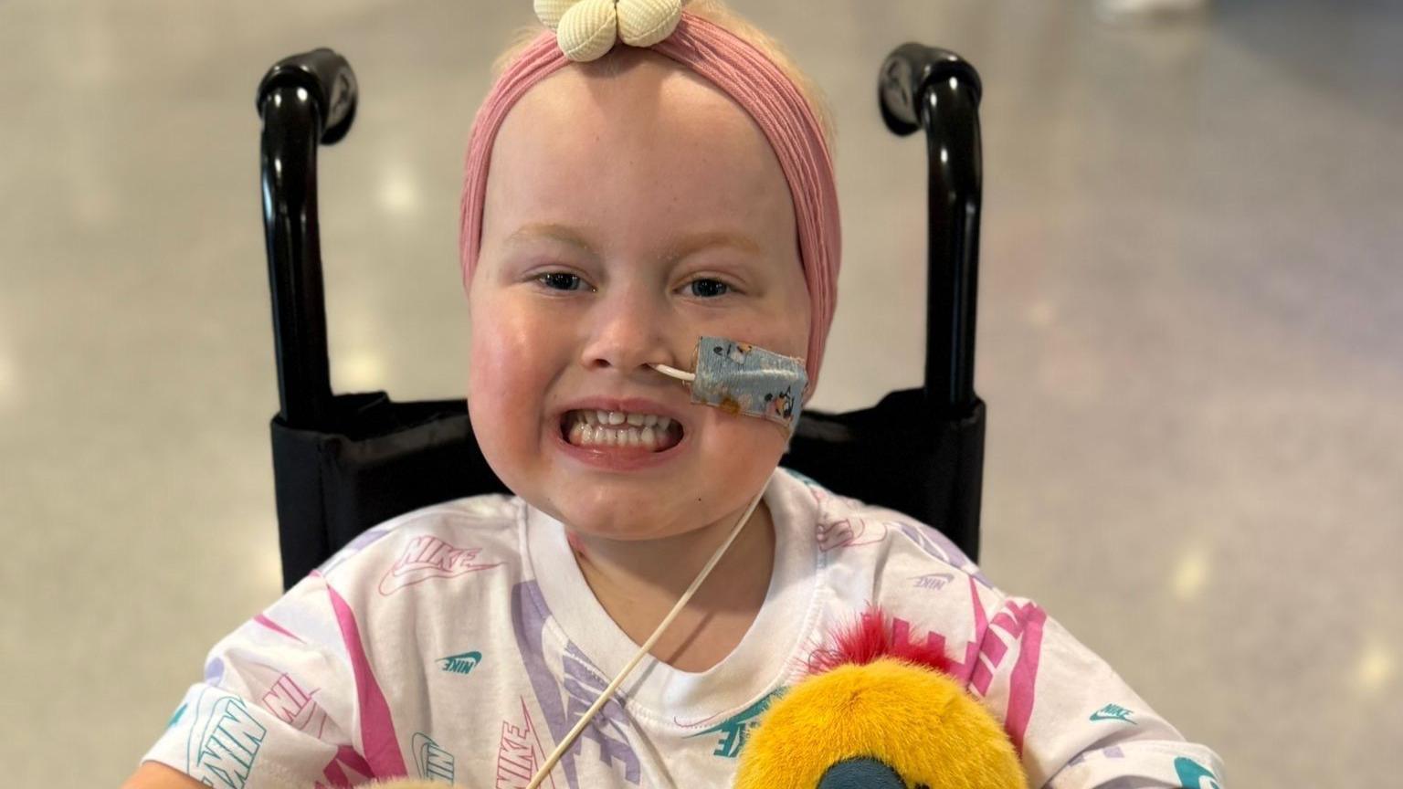 Eliyah, in hospital, smiling at the camera, in a wheelchair with a tube in her nose
