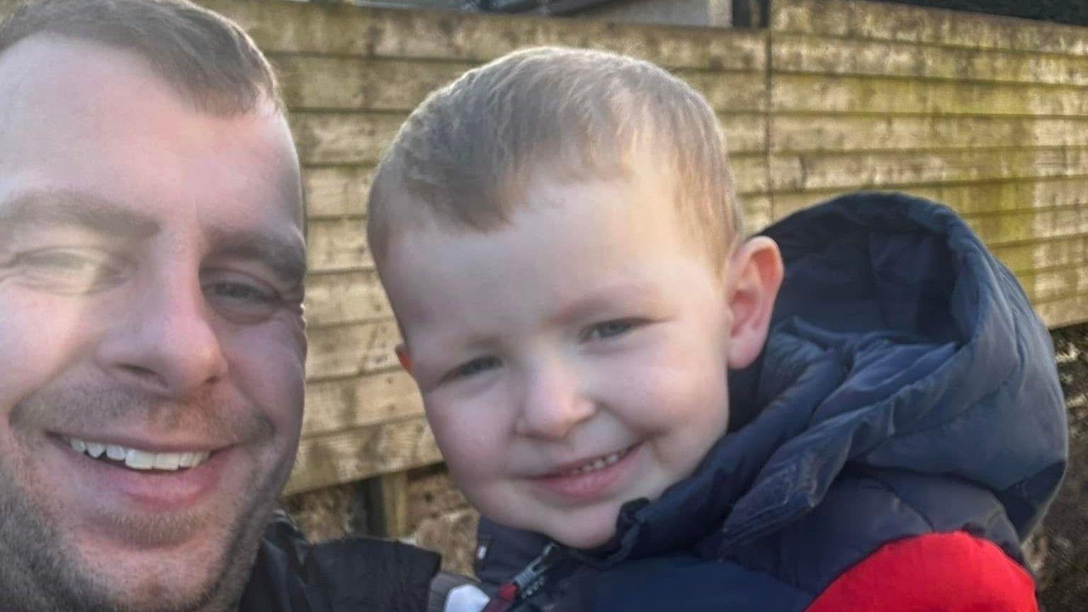 A man holds a young boy, both are smiling at the camera