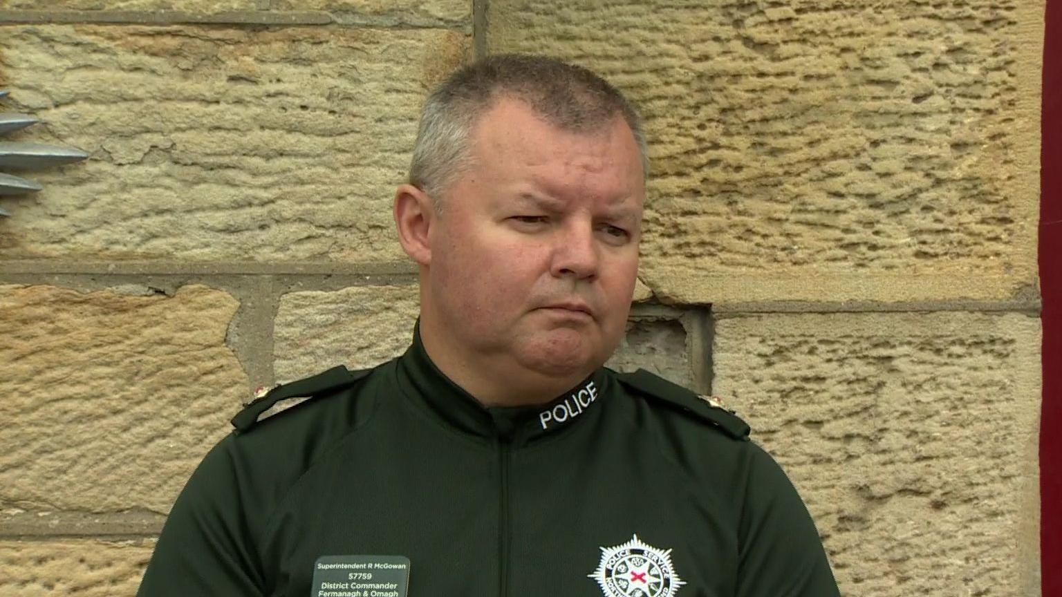 Supt Robert McGowan speaking to reporters at a press conference, He has short, grey hair and is wearing a green police t-shirt.