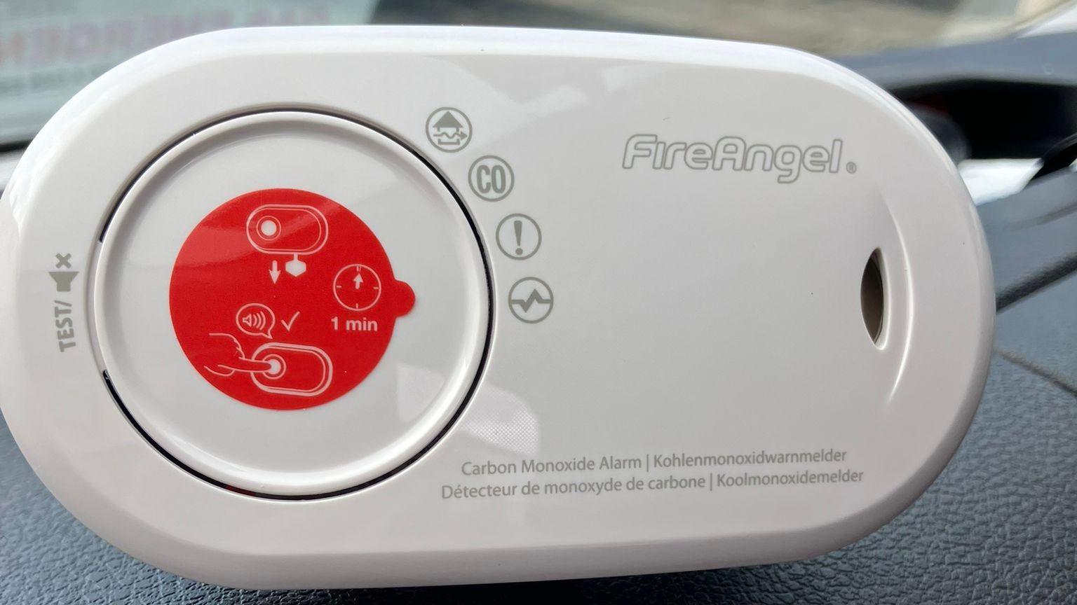 A carbon monoxide alarm by the brand Fire Angela, a white device with a timer sat on a car dashboard.