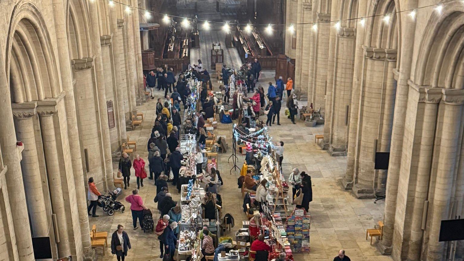A picture of the market taken from above inside the Cathedral - with people lining up to buy and view items along white desks placed in lines.