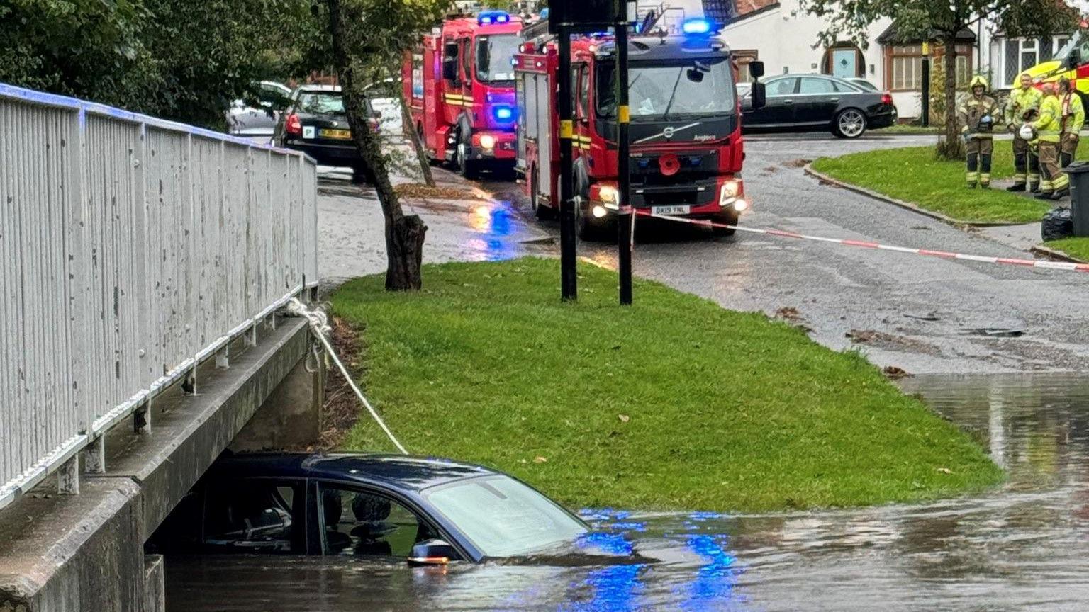 Car submerged under water with fire engines in the background