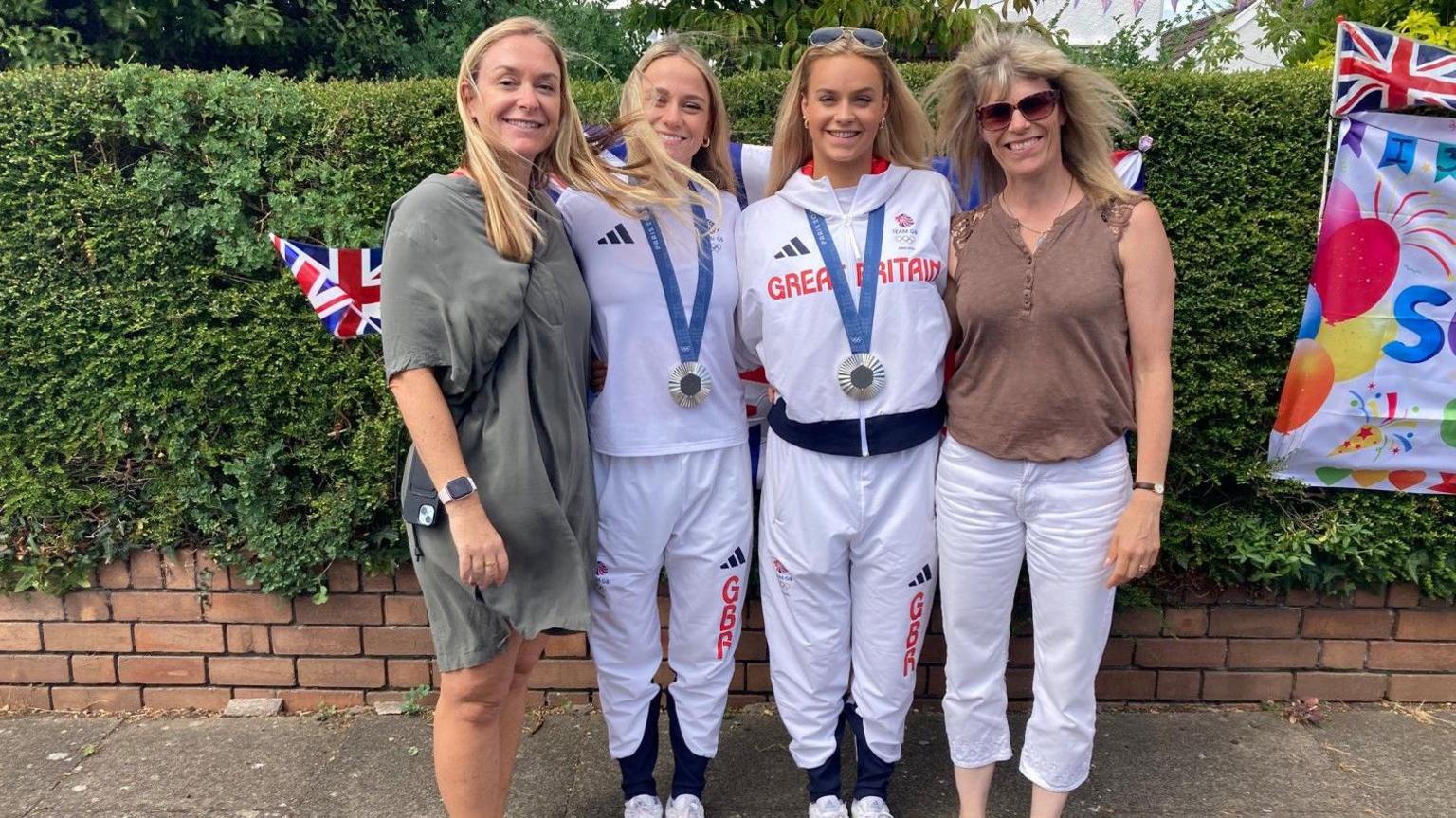 Karen (left), Isabelle (second left), Kate (third) and Kate's mum smiling at the camera outside in front of a garden hedge