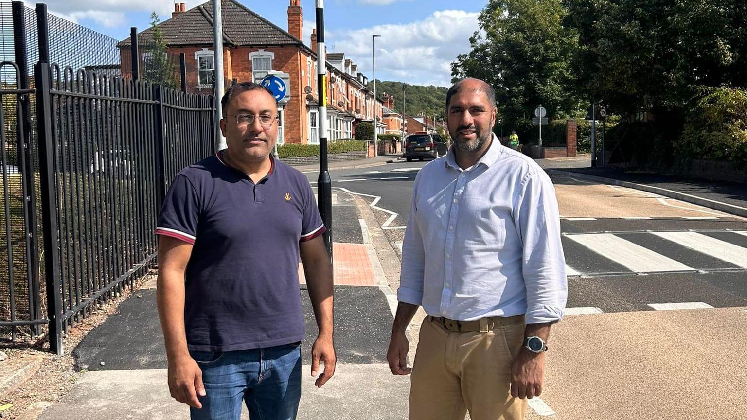 Councillors Jabba Riaz and Atif Sadiq standing together in front of a zebra crossing in Wyld's Lane, Worcester. 